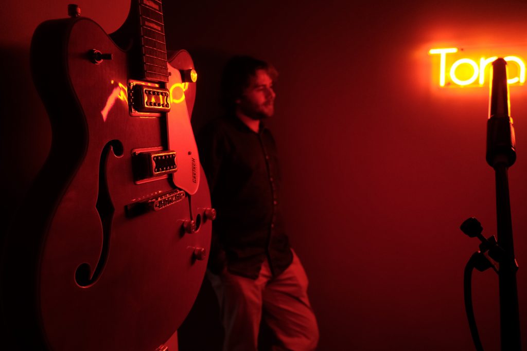 Image of a songwriter stood next to a guitar